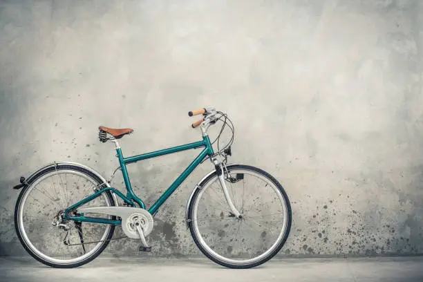 Photo of Retro bicycle with aged brown leather saddle from circa 90s front concrete wall background. Vintage old style filtered photo