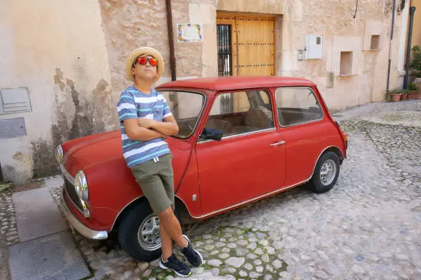 Photo of 12 years old boy and vintage red car on narrow street