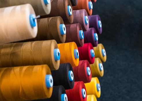 Colourful embroidery thread spool using in garment industry, row of multi coloured yarn rolls, sewing material selling in the market