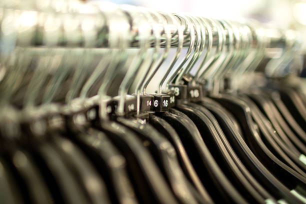 Row of empty clothes hangers on a rail with various woman’s sizes on.