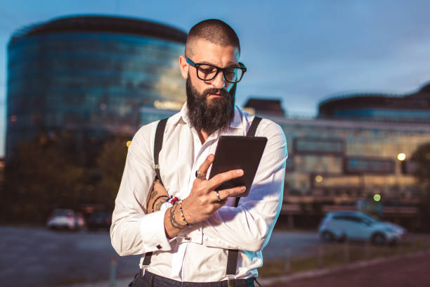 istock Photos Smiling bearded man in white shirt is using digital tablet 1055459504