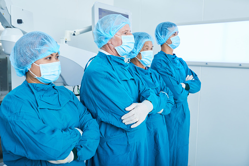 Side view of surgical team in masks keeping arms crossed and looking away while standing in operating theatre together