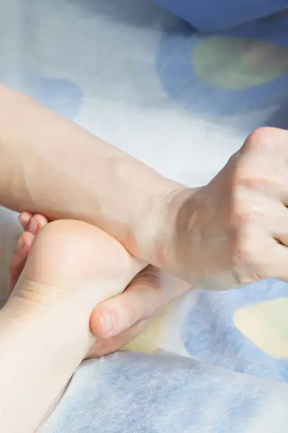 Masseuse making child foot massage with arm. Closeup vertical shot