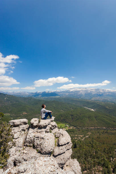Young traveler sitting at the edge, beautiful valley in front of him.