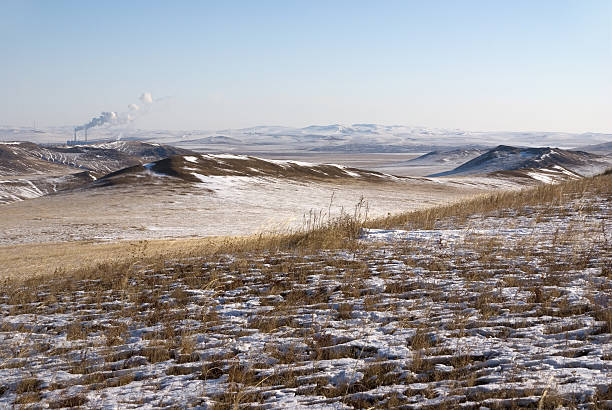 Snow-covered steppe with mountains on the horizon. Mountain pasture covered with snow. Bushes of autumn grass stick out from under the snow.