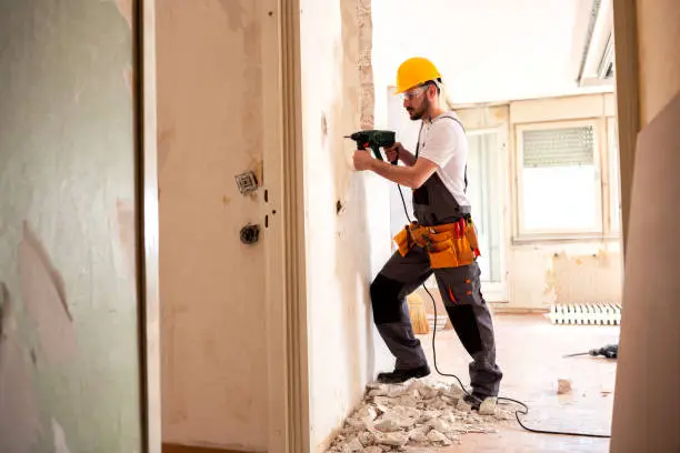 Experienced worker using hammer drill for tearing down a wall structure
