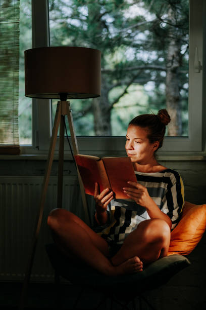istock Young woman reading a book at home by the window 1055479728