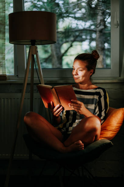 istock Young woman reading a book at home by the window 1055479730