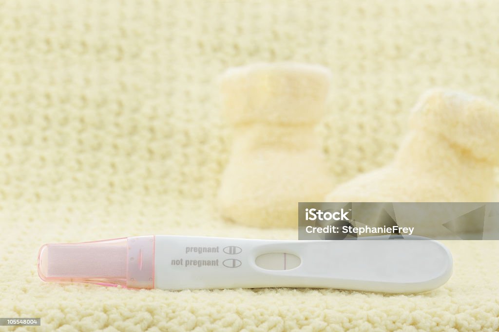 A pink and white pregnancy test displaying a negative result Negative pregnancy test with little cute baby booties in the background. Negative Emotion Stock Photo