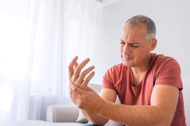 An injured hand will put an end to most workouts Photo of Mature man suffering from wrist pain at home while sitting on sofa during the day. Clenched painful hands hand massage photos stock pictures, royalty-free photos & images