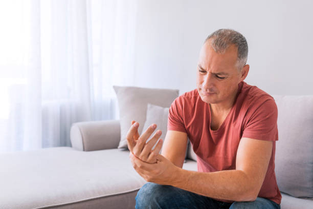 Typing all day has made my wrists stiff Photo of Mature man suffering from wrist pain at home while sitting on sofa during the day. Clenched painful hands hand massage photos stock pictures, royalty-free photos & images