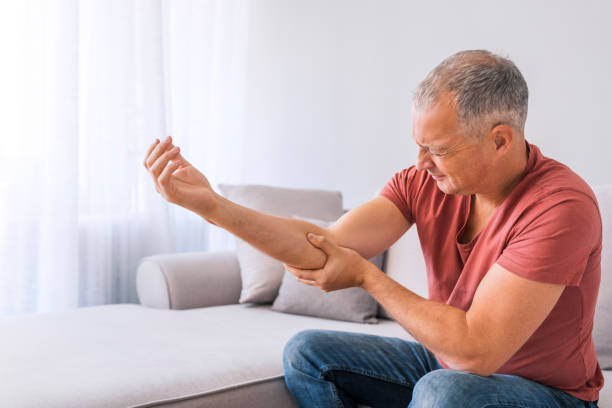 Where is this sharp pain coming from? People, healthcare and problem concept - Photo of unhappy mature gray hair man suffering from elbow pain at home while sitting on sofa during the day. rough hands man stock pictures, royalty-free photos & images