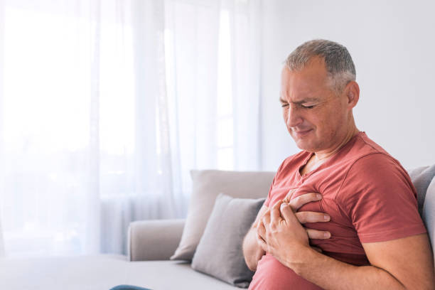 Chest pain is an indicator of a possible heart attack Severe heartache, man suffering from chest pain, having heart attack or painful cramps, pressing on chest with painful expression. Photo of Mature man suffering from chest pain at home during the day. endocarditis stock pictures, royalty-free photos & images