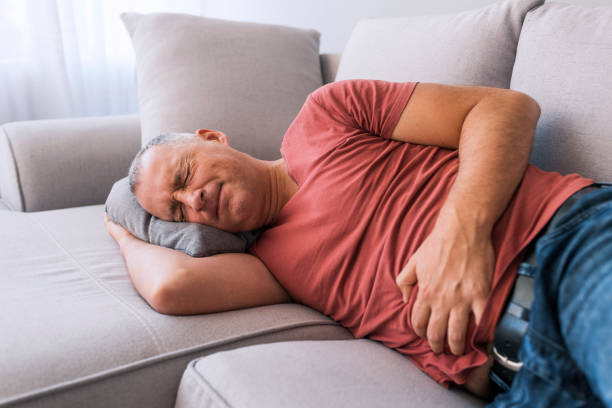 Man suffering from stomachache Photo of Senior man with stomach pain. Mature Caucasian gray hair man stomachache, pressing on stomach with painful expression, laying on sofa at home, food poisoning stock pictures, royalty-free photos & images