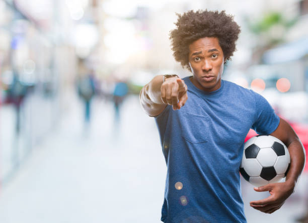 afro americano homem segurando uma bola de futebol isolada fundo apontando com o dedo para a câmera e você, sinal de mão, gesto positivo e confiante da frente - football human hand holding american football - fotografias e filmes do acervo