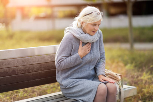 senior woman suffering from chest pain while sitting on bench - chest pain imagens e fotografias de stock