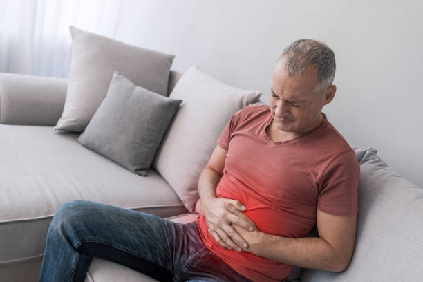 He needs a quick pain reliever Photo of Senior man with stomach pain. Mature Caucasian gray hair man stomachache, pressing on stomach with painful expression, sitting on sofa at home, gastroesophageal reflux disease photos stock pictures, royalty-free photos & images