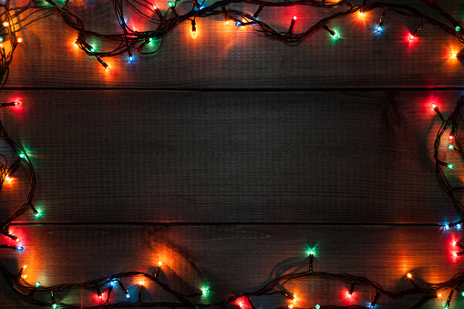 Glowing Christmas garland on brown wooden board as background with copy space.