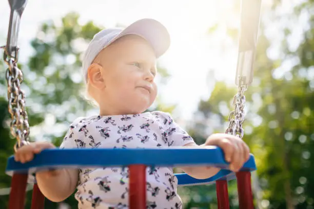 Baby boy playing in playground area. Portrait of smiling toddler looking away with happy face, having fun. Swaying on sunny summer day outdoors.