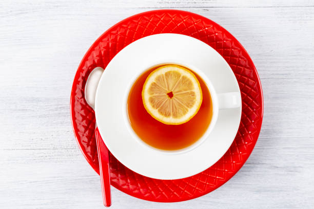 istock Tea with lemon in a white mug on a red plate. On a wooden table. Tea spoon. Top view. 1055520554