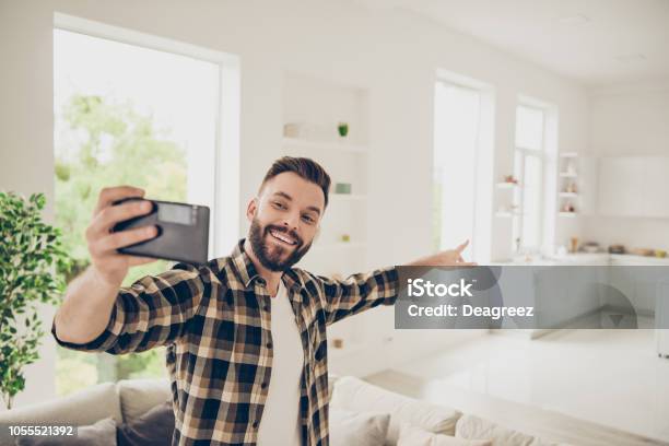 Apartment Purchase Concept Lets Go And Ill Show You My House Young Man Make Call On Front Camera Of Modern Smartphone Standing In The Middle Of A Light Room In His Brown Stylish Trendy Shirt Stock Photo - Download Image Now