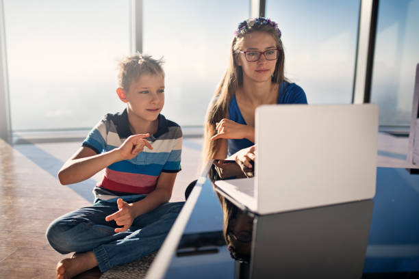 Brother and sister sitting modern apartment and learning sign language online. \nNikon D850