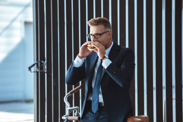 istock middle aged businessman sitting on bicycle and eating hamburger 1055525020