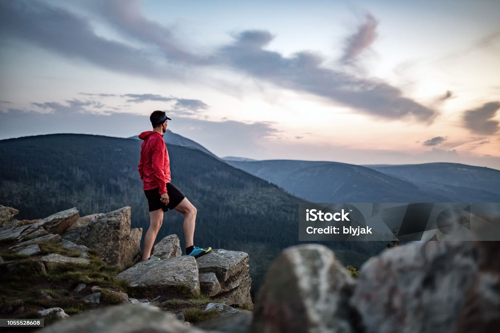 Man celebrating sunset looking at view in mountains Man celebrating sunset looking at view in mountains. Trail runner, hiker or climber reached top of a mountain, enjoy inspirational landscape on rocky trail Karkonosze, Poland Mountain Stock Photo