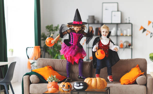 glückliche kinder in kostümen der hexe und vampir bereiten nach hause für halloween - child jumping vegetable food stock-fotos und bilder