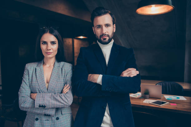 istock Two serious modern professional stylish elegant classic leaders, partners in jackets, beautiful adorable lady boss and bearded man, folded arms at industrial work place, station 1055531642