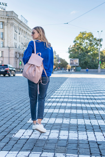 woman looking back goes on a pedestrian crossing on the pavement, rear view