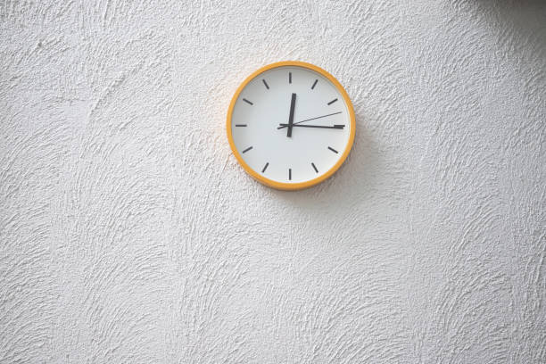 istock yellow plastic clock on concrete wall show time  on mid day, free copy space for text. 1055535544