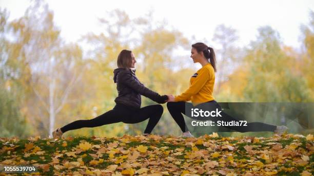 Girls Warming Up Before Training In Park Stretching Towards Each Other Smiling Stock Photo - Download Image Now