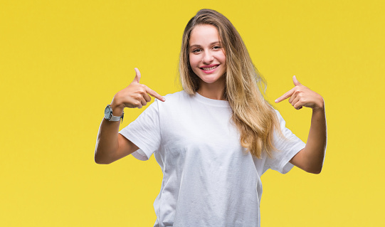 Young beautiful blonde woman wearing casual white t-shirt over isolated background looking confident with smile on face, pointing oneself with fingers proud and happy.