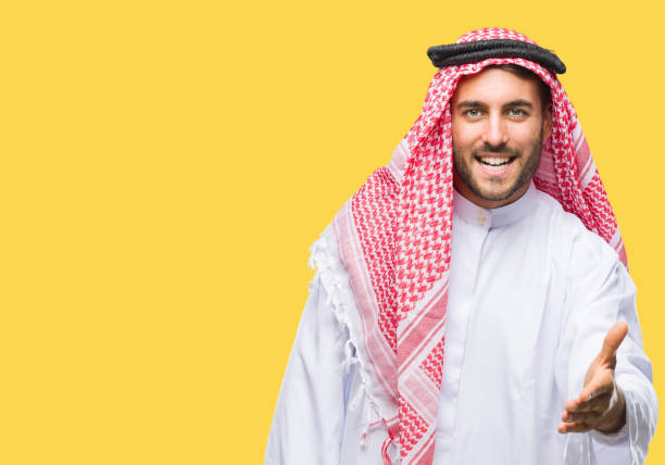istock Young handsome man wearing keffiyeh over isolated background smiling friendly offering handshake as greeting and welcoming. Successful business. 1055547446