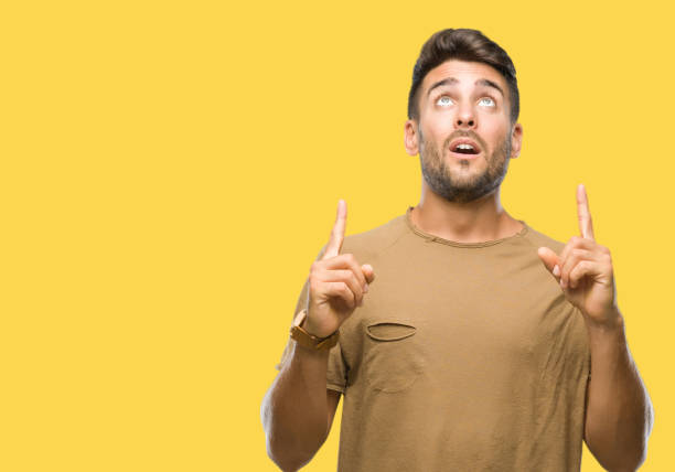 istock Young handsome man over isolated background amazed and surprised looking up and pointing with fingers and raised arms. 1055547490