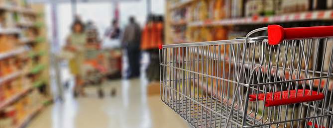 Supermarket shopping. Shopping cart, empty, with red handle on blur grocery background. 3d illustration