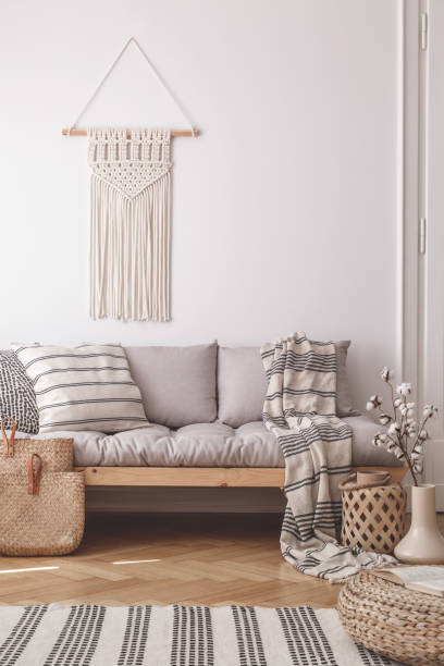 istock Beige, handmade macrame on a white wall above a couch with a striped linen pillow in a natural living room interior 1055555420