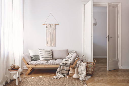 Sunlit living room interior with open door, herringbone parquet floor, natural, beige textiles and white walls