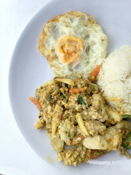 istock Stir-fried seafood, prawn and squid with yellow curry powder with rice and fried egg in white plate on white background. Thai style food. 1055555986