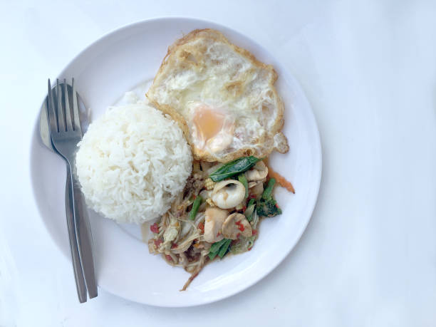 istock Fried spicy fried seafood with basil leaves and mixed vegetable and fried egg on jasmine rice in white dish. Thai style food. 1055556466