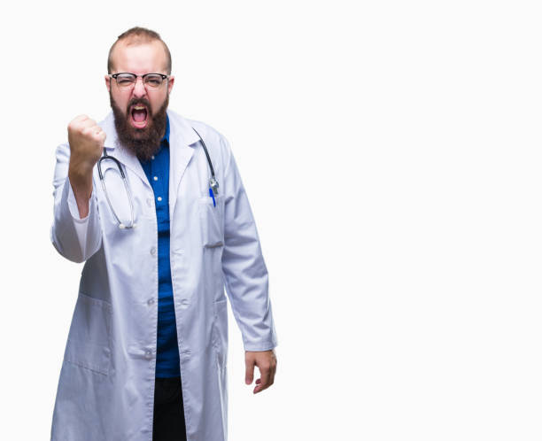 Young caucasian doctor man wearing medical white coat over isolated background angry and mad raising fist frustrated and furious while shouting with anger. Rage and aggressive concept. Young caucasian doctor man wearing medical white coat over isolated background angry and mad raising fist frustrated and furious while shouting with anger. Rage and aggressive concept. fist human hand punching power stock pictures, royalty-free photos & images