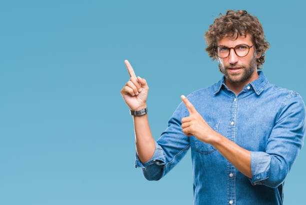 istock Handsome hispanic model man wearing glasses over isolated background smiling and looking at the camera pointing with two hands and fingers to the side. 1055560086