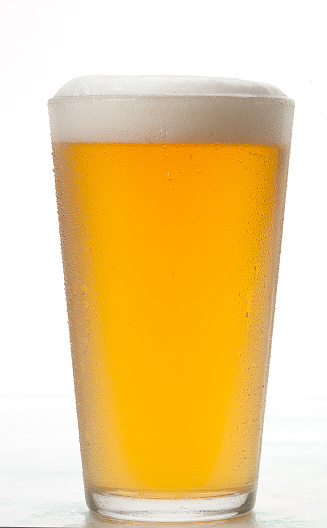 Sparkling beer in a glass. Little head on top of tall beer glass surrounded with two unopened brown bottles. Vertical still life on grey background.