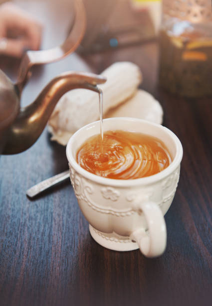istock Old-style copper kettle pouring tea to cup on wooden table 1055571118