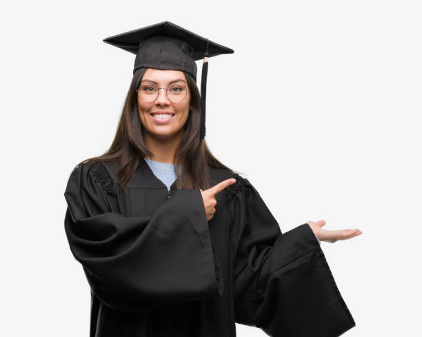 istock Young hispanic woman wearing graduated cap and uniform amazed and smiling to the camera while presenting with hand and pointing with finger. 1055578012
