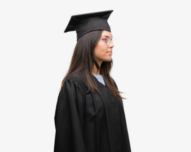 istock Young hispanic woman wearing graduated cap and uniform looking to side, relax profile pose with natural face with confident smile. 1055578026