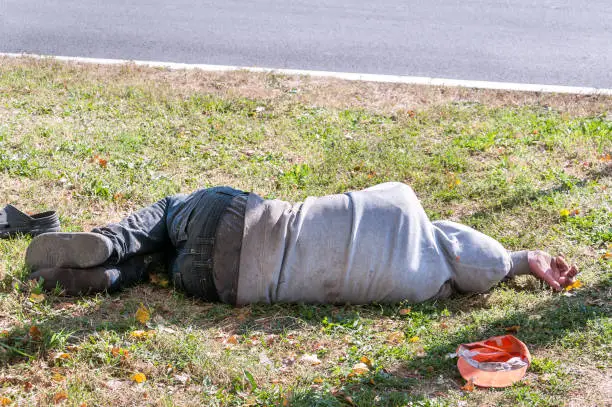 Photo of Old dirty drunk or drug addict barefoot homeless or refugee man sleeping on the grass in the street social documentary concept