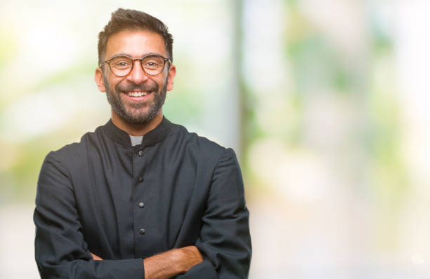erwachsenen hispanische katholischer priester mann über isolierte hintergrund glückliches gesicht lächelnd mit verschränkten armen in die kamera schaut. positiver mensch. - priester stock-fotos und bilder