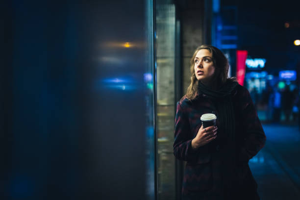 Young beautiful woman standing downtown at night with a coffee to go.
